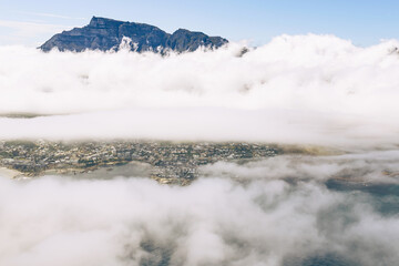 Aerial view of mountain peaks emerging from a dense blanket of clouds covering a city. Scenic natural phenomenon for travel and nature concepts.