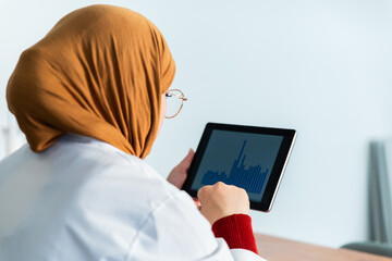 Muslim female scientist in hijab analyzing data and charts on digital tablet in the laboratory