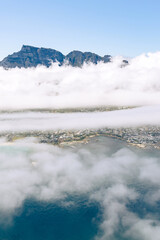 Aerial view of mountain peaks emerging from a blanket of white clouds above a coastal city and ocean, showcasing natural scenery