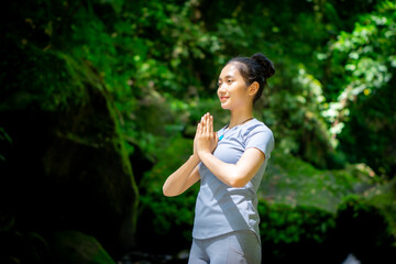 Asian woman enjoying yoga alone in nature with large mossy rocks and flowing river water in the forest