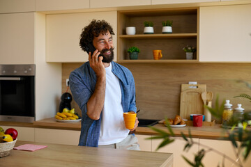Smiling Man Talking On Phone While Drinking Coffee In Kitchen