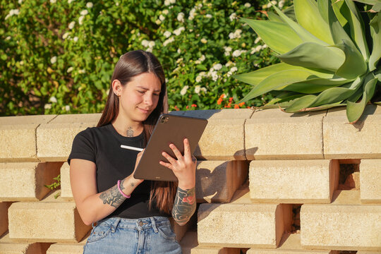 Young woman creating digital art with a tablet and stylus in a sunny outdoor setting