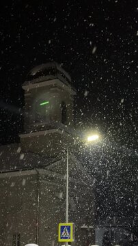 A winter evening street. A captivating shot of heavy, dense snowflakes falling rapidly at night. The snow is brightly lit by the sharp, concentrated light of a street lamp, 