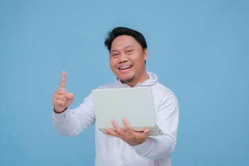 Young Asian man pointing at his laptop with happy smiling expression on turquoise blue background 