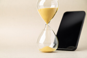Close-up of an hourglass with golden sand standing in front of a blurred smartphone. Concept of digital detox, time management, screen time addiction, mental wellness, and prioritizing real life.