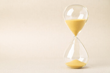 Minimalist close-up of a glass hourglass with flowing golden sand on a neutral background. A conceptual image representing time passing, deadlines, waiting, patience, and effective time management.