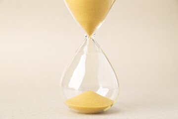Extreme close-up of golden sand falling inside an hourglass on a neutral background. Conceptual image for time running out, deadlines, aging, life cycles, patience, and mindful time management.