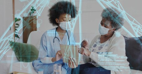 Showing nurse in blue scrubs explaining tablet on sofa at home, with stethoscope, surgical masks