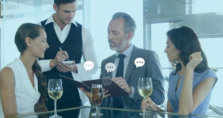 Discussing menu, suited man and coworkers holding wine glasses at bar, with speech bubble graphics