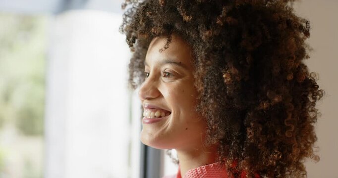 Woman gazing out through big glass window, smiling in sunlight and appreciating foliage, copy space