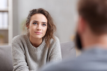 Two adults sitting in psychological group session, one speaking calmly, one listening, bright neutral interior, stock photo style.