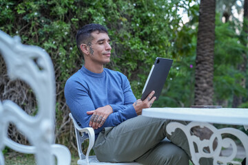 Obraz premium Young adult man sitting outdoors, enjoying digital communication on a tablet