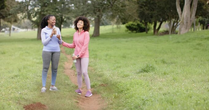 Diverse female friends jogging park stopping sharing coffee and drinking water bottles, copy space