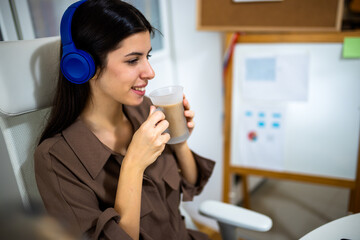 Young woman enjoying music on headphones in her home office. Cozy workspace with laptop and coffee, ideal for relaxation, work-from-home, and lifestyle concepts.