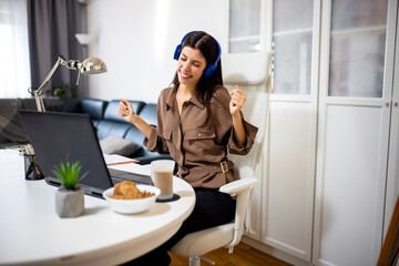 Young woman enjoying music on headphones in her home office. Cozy workspace with laptop and coffee, ideal for relaxation, work-from-home, and lifestyle concepts.