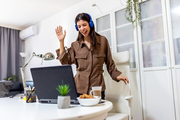 Young woman playing on her laptop while listening to music on headphones. Fun, digital leisure, and cozy home lifestyle, perfect for gaming, productivity, and relaxation themes.
