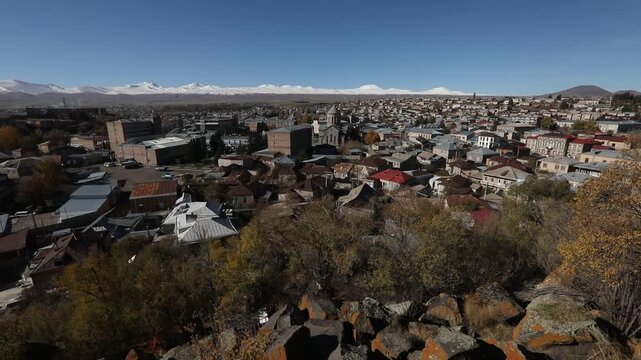 Panoramic view of Gyumri, Armenia, featuring traditional architecture. Majestic snow-capped peaks of Mount Aragats rise in the background under a clear blue sky during a sunny autumn day.

