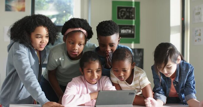 Diverse classmates leaning around tablet on low table at school, watching content and collaborating