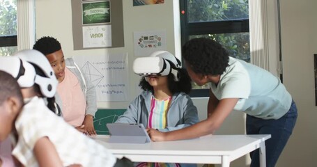 African American children at classroom desk, standing peer leaning, guiding VR child using tablet - Powered by Adobe