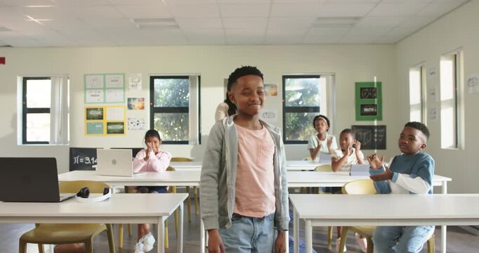 African American class clapping in class, teacher with tablet urging preteen boy bowing and walking