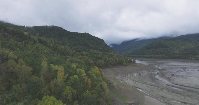 Aerial drone of a braided riverbed and wide valley floor in the Pyrenees near Huelva, Spain and France, moody clouds and mist hugging the mountains
