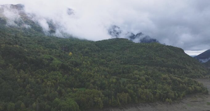 Aerial drone view of fog drifting over Pyrenees mountains near Huelva, Spain and France, wide valley with braided riverbed and dramatic cloud cover