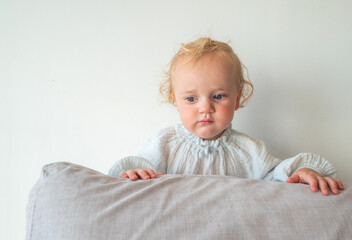 Fototapeta premium A baby is standing on a pillow and looking at the camera