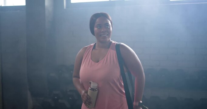 African-American woman entering gym holding bottle, bag, checking smartwatch preparing for workout