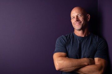 Obraz premium A confident bald man standing against a deep purple background, smiling with strength and optimism.
