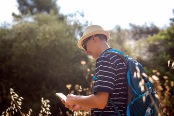 Teenage boy hiking in summer while checking his phone for navigation. Modern outdoor lifestyle combining technology, travel, and exploration in nature.
