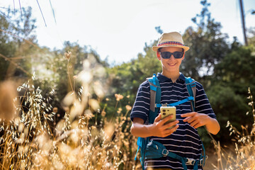 Teenage boy hiking in summer while checking his phone for navigation. Modern outdoor lifestyle combining technology, travel, and exploration in nature.