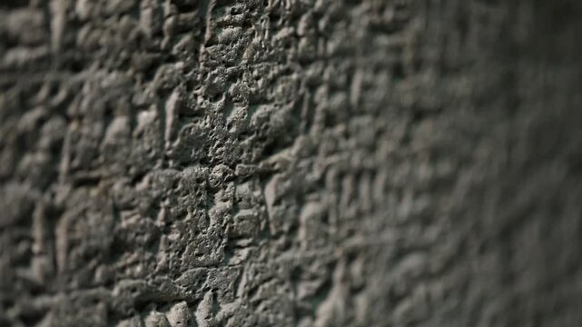Extreme close-up vertical panning shot of an ancient dark basalt stone surface with carved Hebrew inscriptions, revealing the rough texture and historical detail of this archaeological artifact.

