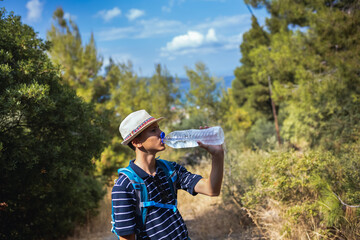 Teenage boy drinking water from a plastic bottle during a summer hike. Hydration, outdoor adventure, and active lifestyle in nature, perfect for travel and fitness concepts.