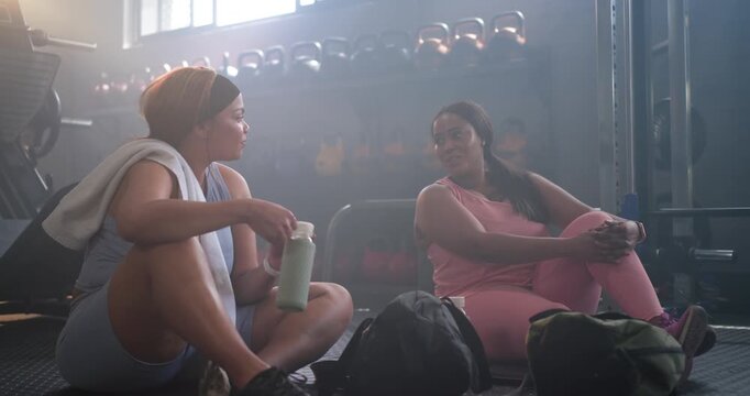 Diverse female friends sitting at gym, left woman grabbing phone, taking selfie with water bottle