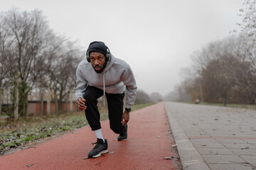 Fototapeta premium Focused athletic man in starting position on an outdoor running track, preparing to sprint. Urban fitness training, speed and power workout, healthy active lifestyle