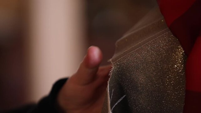 A close-up shot of a craftsman's hands sanding the rough edge of a wooden structure. He uses a small wooden tool to smooth the surface in a dim workshop.

