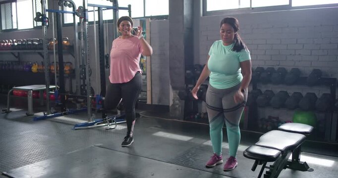 Diverse female friends starting warmup balancing on one leg reaching back pulling heel near weights