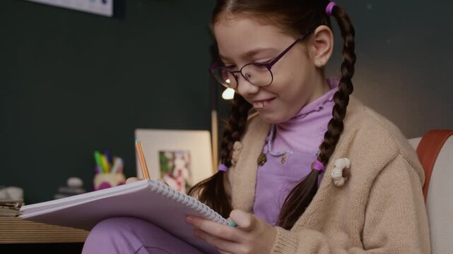 Tilt up shot of inspired Caucasian girl child in eyeglasses focusing on homework at cozy desk, contemplating about math problem or writing creative essay