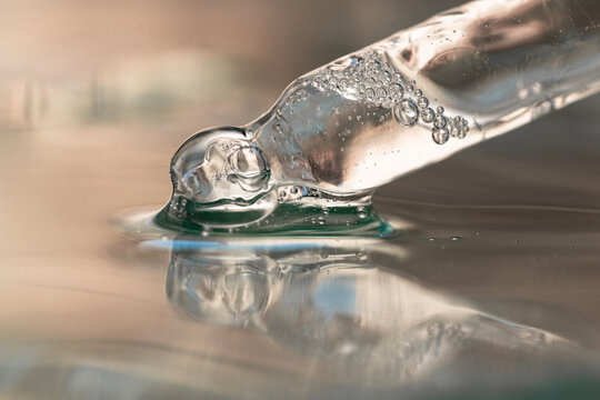 Glass pipette with transparent serum, hyaluronic acid close-up on beige background, front view.