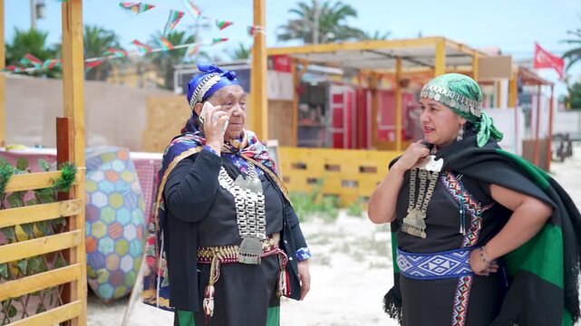 Elderly mapuche woman wearing traditional clothing and silver jewelry talking on her smartphone