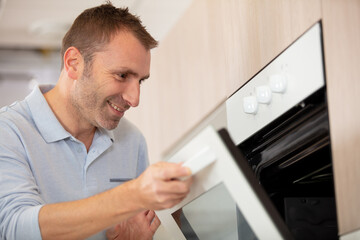 male wearing blue shirt in modern kitchen open oven door