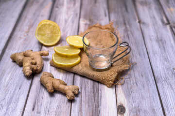 Empty glass tea cup on a dark stone, surrounded by lemon slices, fresh ginger and mint on a rustic wooden table. Natural light and zen-inspired composition