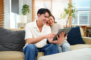 Obraz premium couple sitting on sofa in home playing tablet and relaxing together. They are smiling and enjoy to spend their time together with happiness.