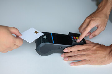 A customer is holding a white credit card with a chip tapping near a point-of-sale (POS) terminal for make contactless payment. People and modern technology concepts.
