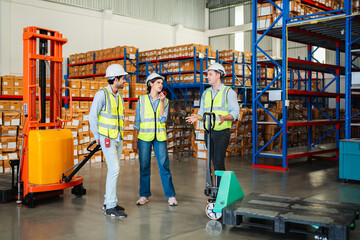 Group of diverse warehouse workers in safety vests and hard hats talking and relaxing in a logistics center with forklift and pallets. Industrial teamwork and storage management concept.