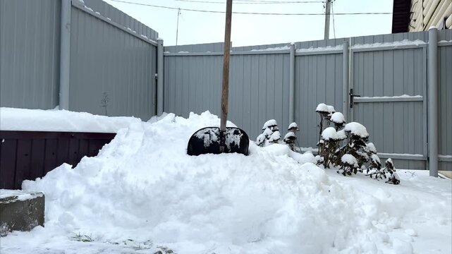 Snow shovel positioned against a snow mound in a backyard, showcasing the accumulation of snow and the need for clearing, highlighting the winter scene and tools