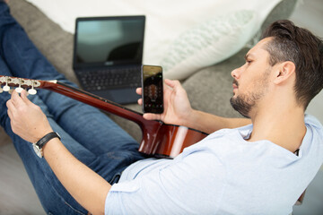 young guitarist hipster at home with guitar tuning using app