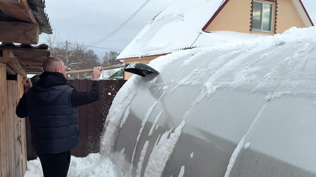 Man shoveling snow off a large curved surface, demonstrating continuous action of snow removal, showcasing effort and technique in a winter setting with visible snow accumulation