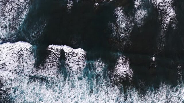 Aerial view of Lanzarote in the Canary Islands, black sand, rust rocky outcrops and reef lines. Powerful waves break, white foam and turquoise streaks show motion.