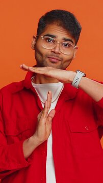 Tired serious upset Indian young man showing time out gesture, limit or stop sign, no pressure, I need more time, take a break, relax, rest, help. Arabian guy isolated on orange studio background